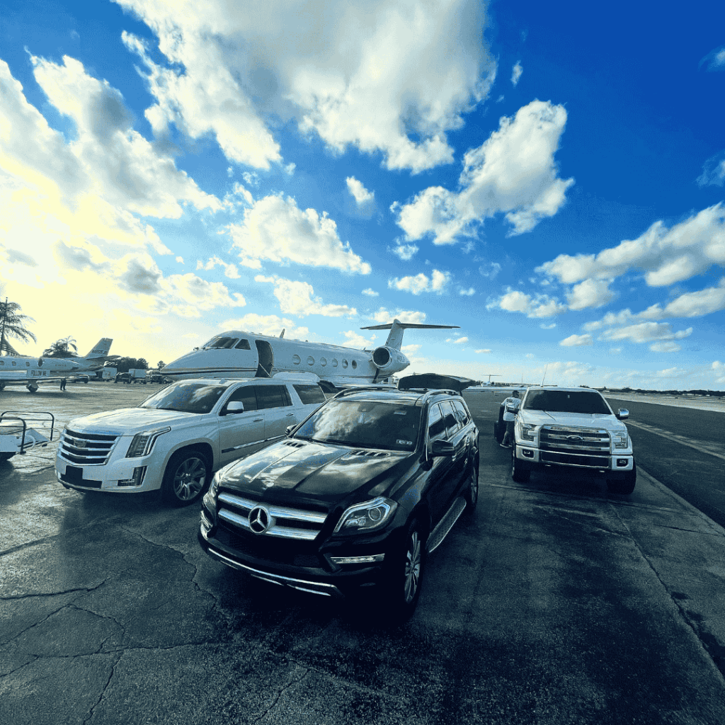 “Luxury private jet on the ramp with black Mercedes SUV, white Cadillac Escalade, and Ford truck for VIP ground transportation under a blue sky