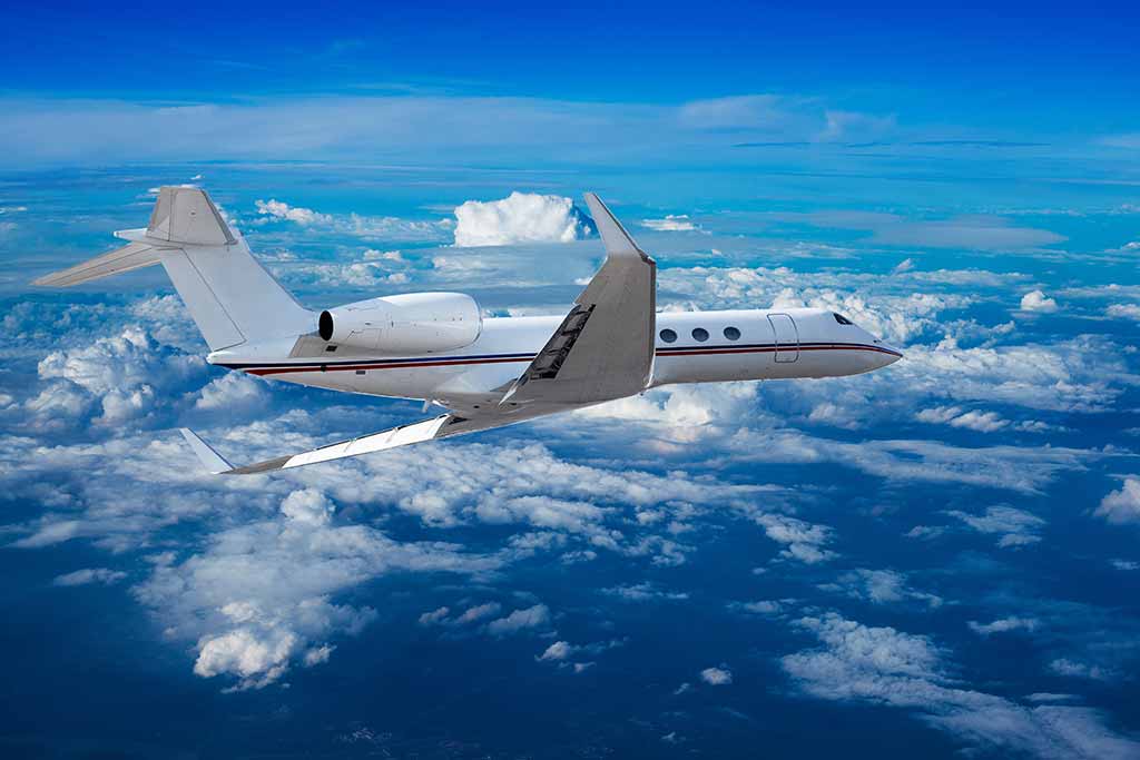 Private jet flying above the clouds, with a clear blue sky in the background.